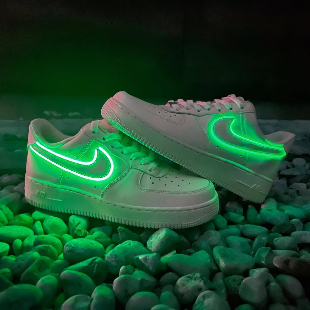Customized Air Force 1 Sneakers with Neon Lights in vibrant green glow on a bed of pebbles.