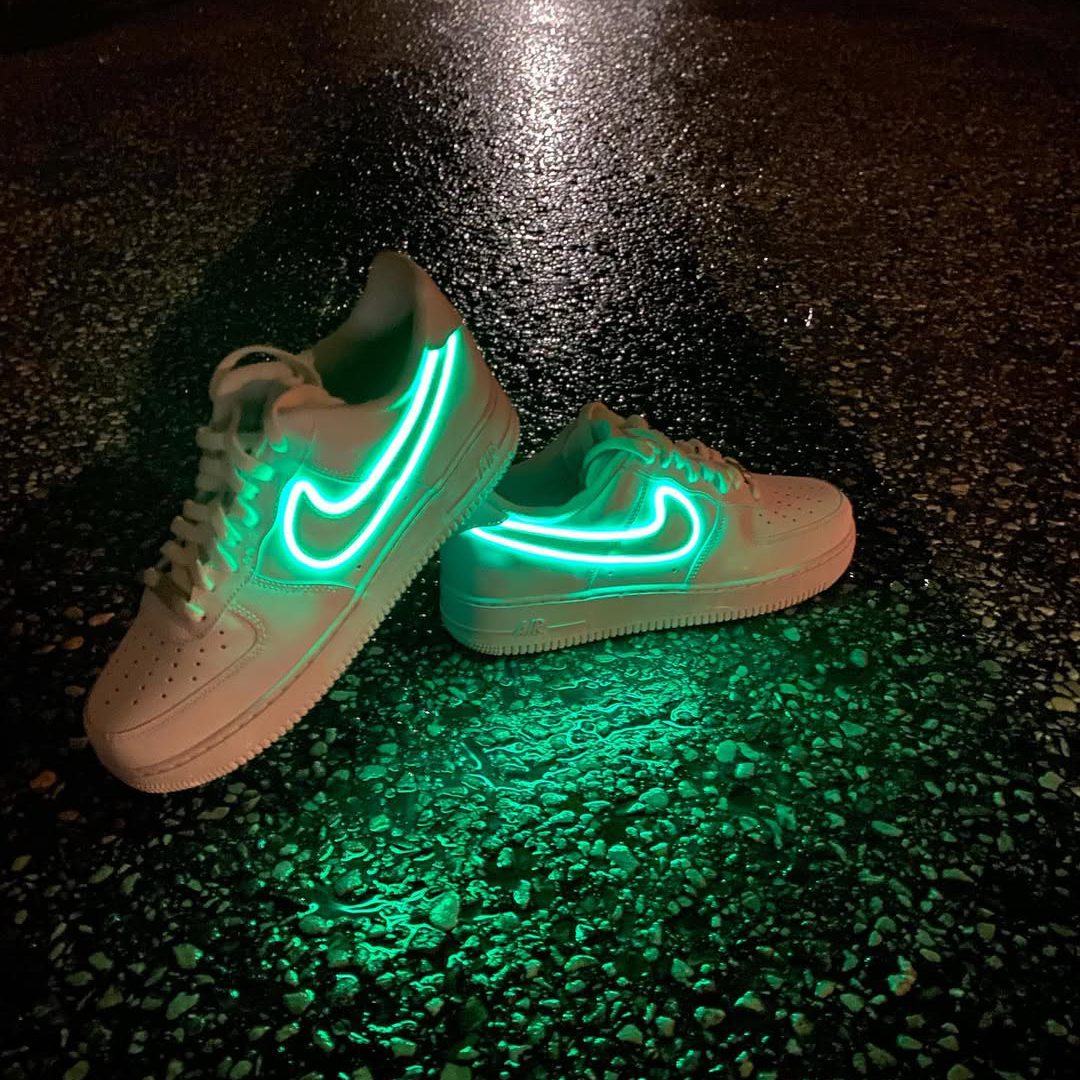 Customized Air Force 1 Sneakers with Neon Lights glowing in vibrant green on a dark reflective surface.